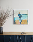 Framed artwork on a wall above a blue cabinet with a vase of branches.