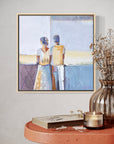 Framed artwork of two people on a wall above a wooden table with decor items.