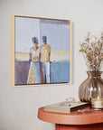 Framed artwork of two people on a wall above a wooden table with decor items.