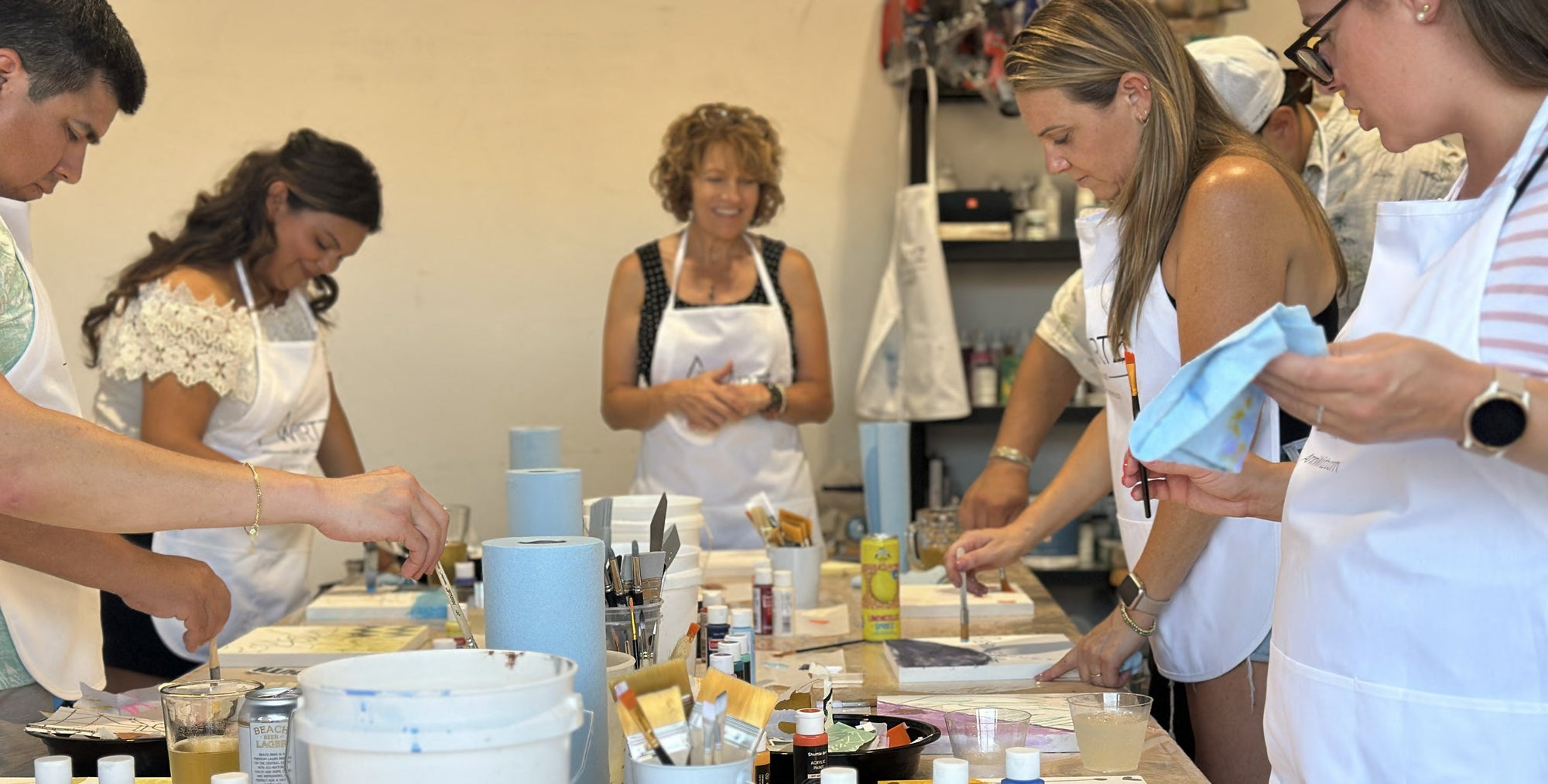 Group of people in an art studio setting with aprons on, at a creativity workshop.