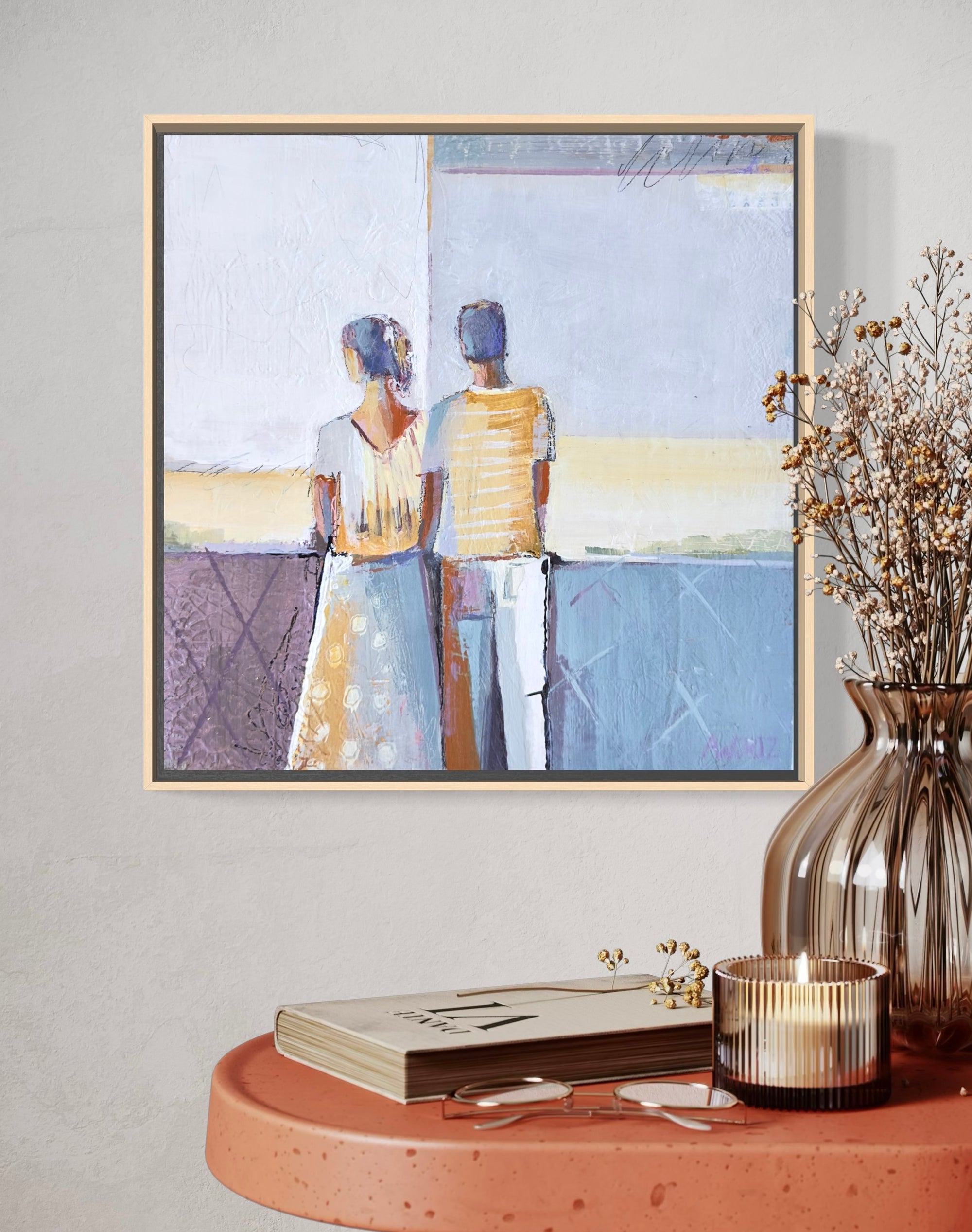 Framed artwork of two people on a wall above a wooden table with decor items.