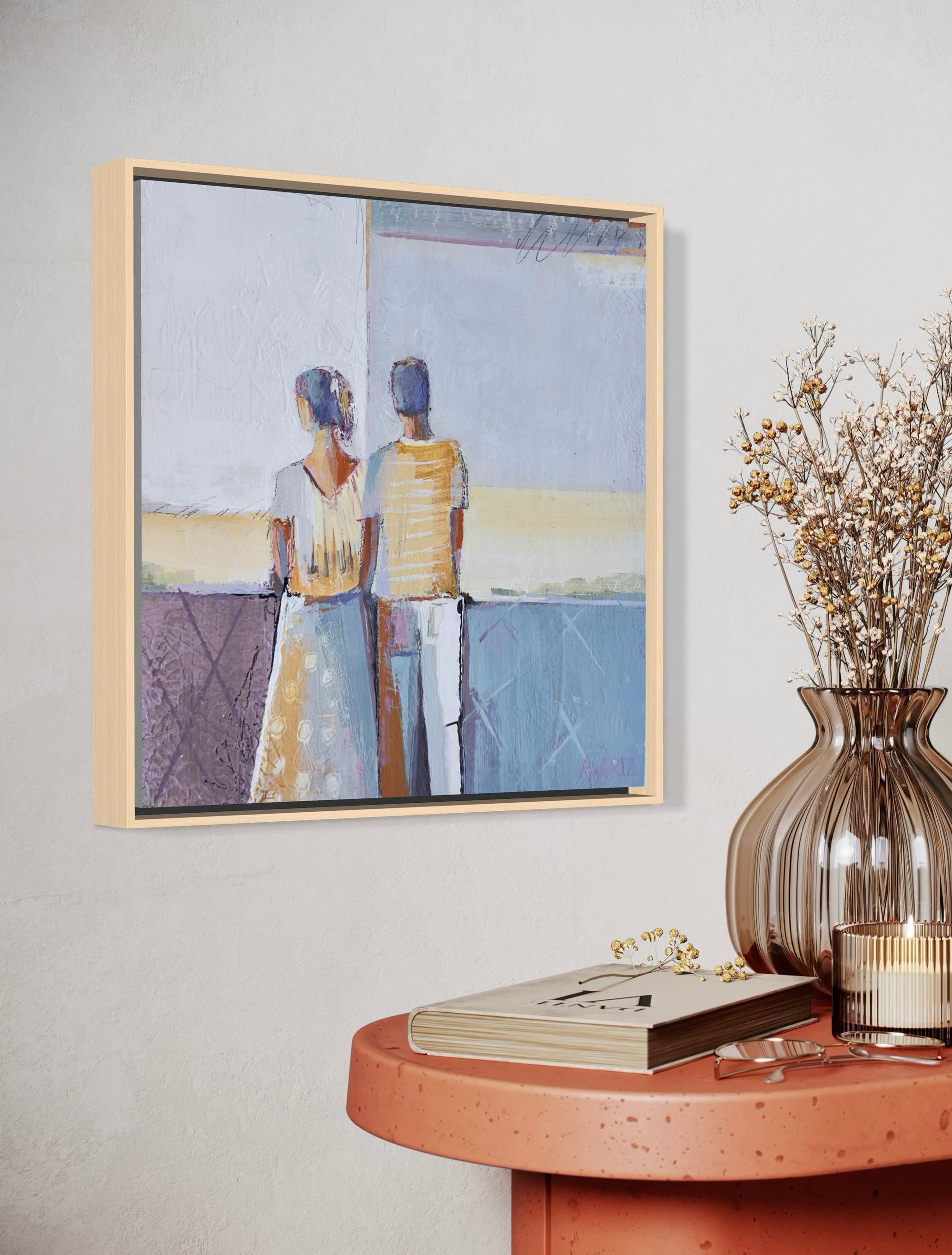 Framed artwork of two people on a wall above a wooden table with decor items.