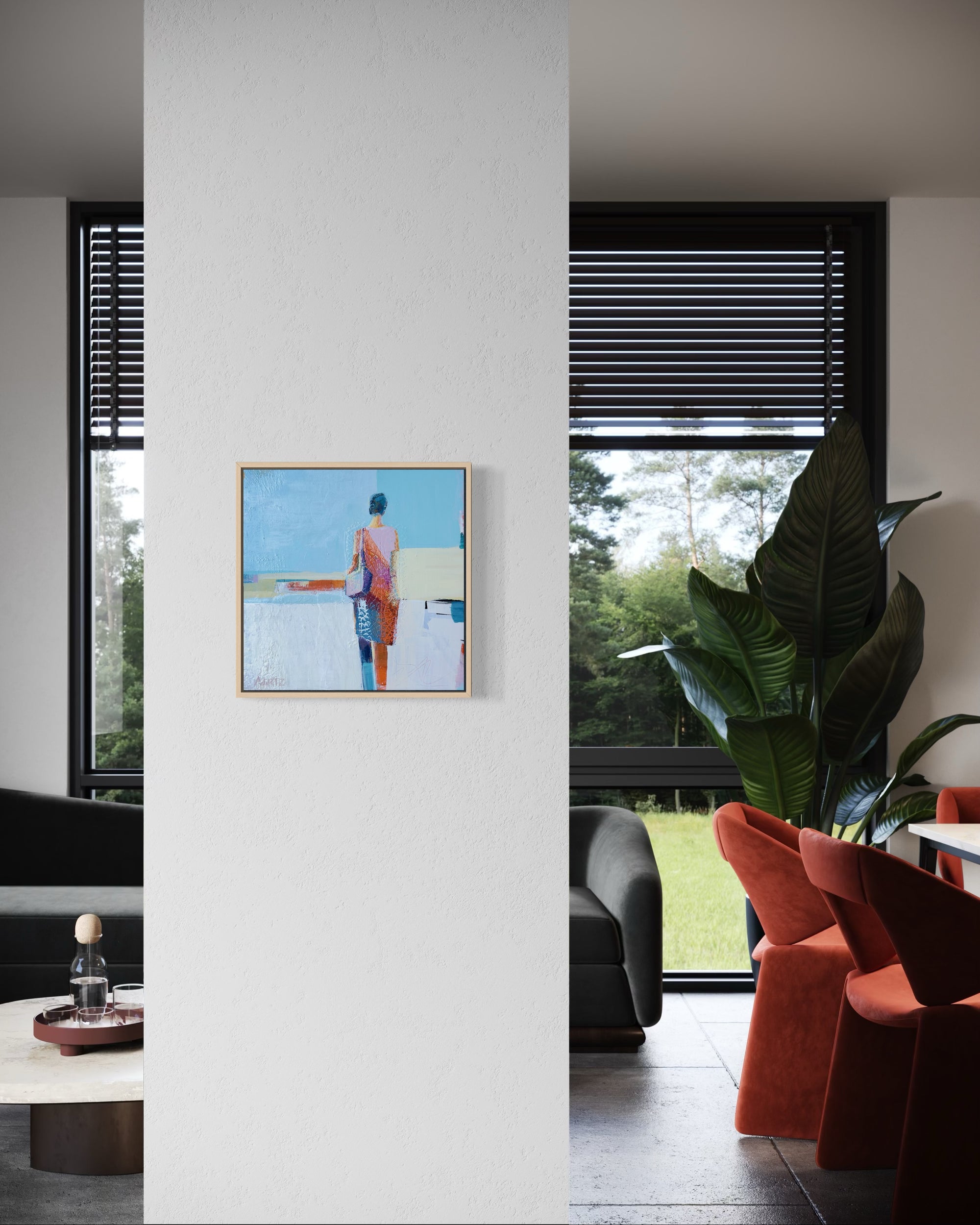 Framed artwork on a white wall in a modern living room with orange chairs and large windows.