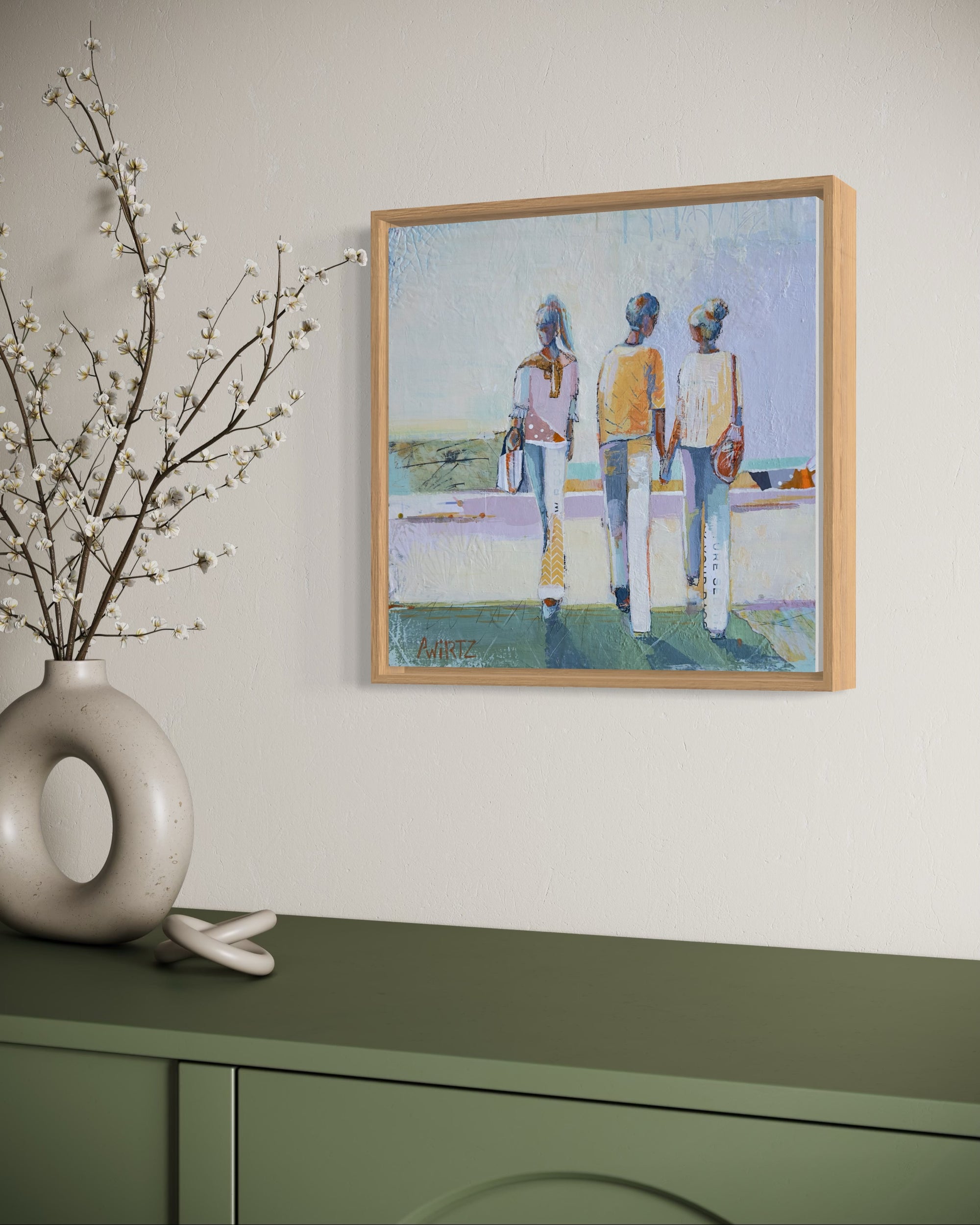 Framed artwork of three people on a wall above a green cabinet with decorative branches.